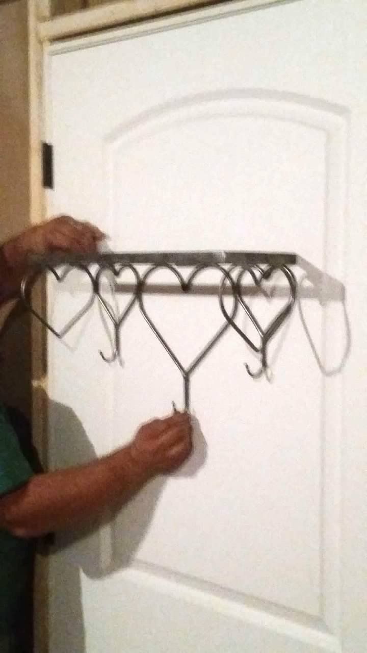 A person is holding a shelf with hooks on it in front of a door.