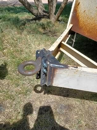 A trailer with a tow hook attached to it is sitting in the grass.