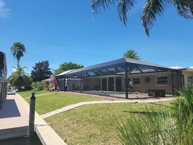 Screened-in patio enclosure with a bright sun, a house, and some trees.