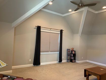 Room with a high ceiling, window with dark curtains, tan walls, and a ceiling fan.