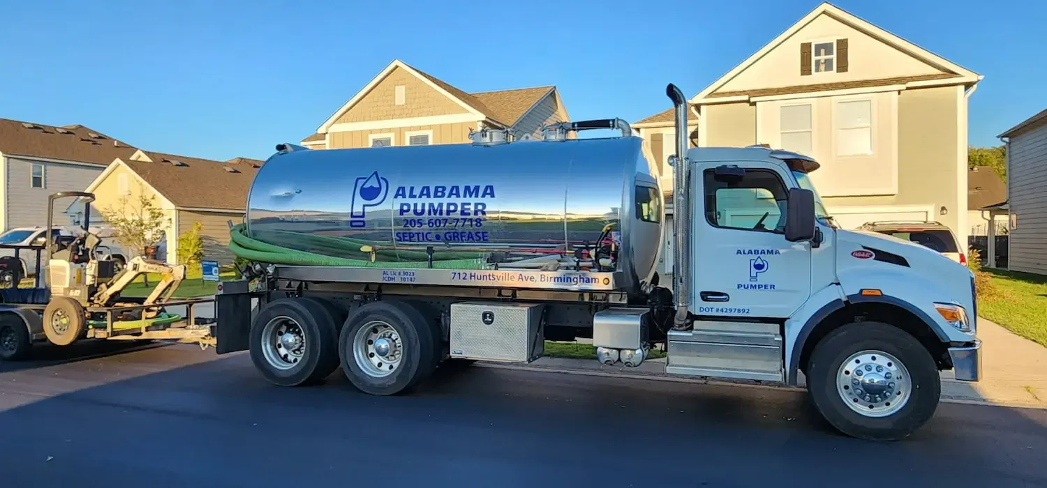 A white Alabama Septic Services tanker truck parked on a residential driveway near a small construction vehicle.
