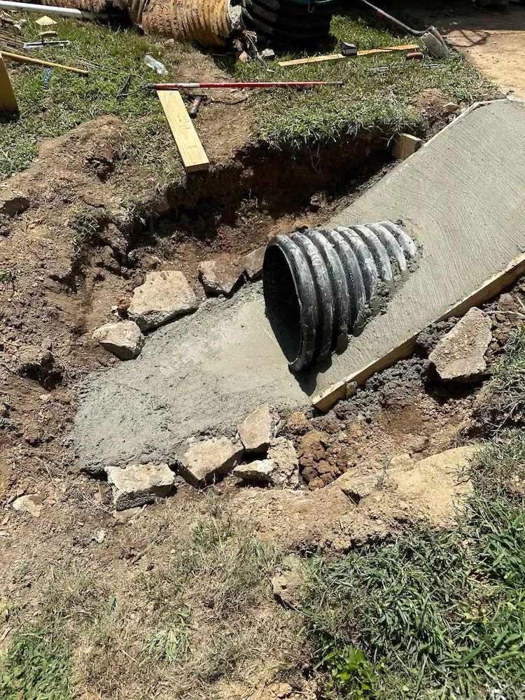 A black corrugated drainage pipe set into a fresh concrete slope within a dirt excavation site.