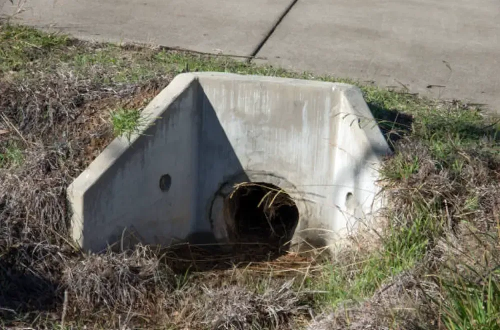 A concrete drainage headwall set into a grassy embankment near a paved sidewalk.