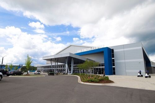 Modern building exterior with a blue entrance, large awning, parking lot, and cloudy sky.