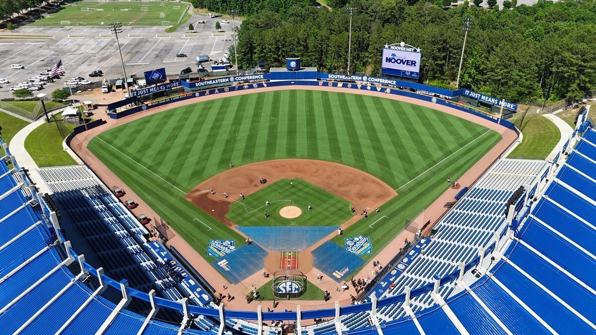 An aerial view of a baseball stadium with blue seating, a manicured green field, and a dirt infield.