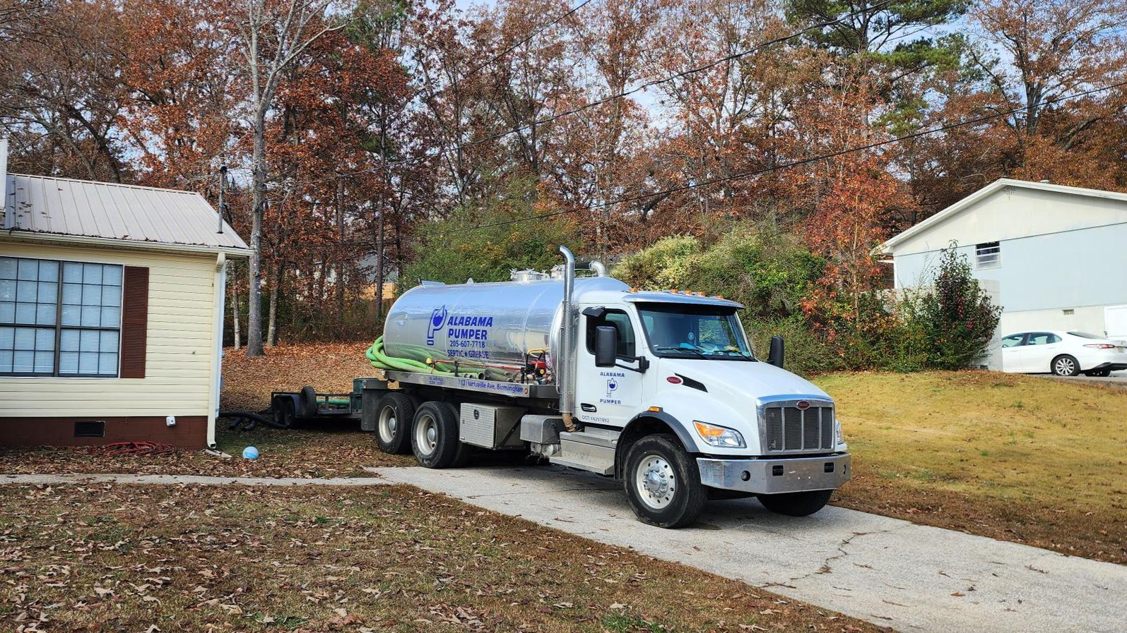 A white fuel delivery truck is parked in a residential driveway on a fall day with fallen leaves on the ground.