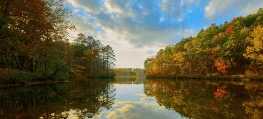 A tranquil lake surrounded by autumn trees with colorful orange and green foliage reflecting on the calm water.