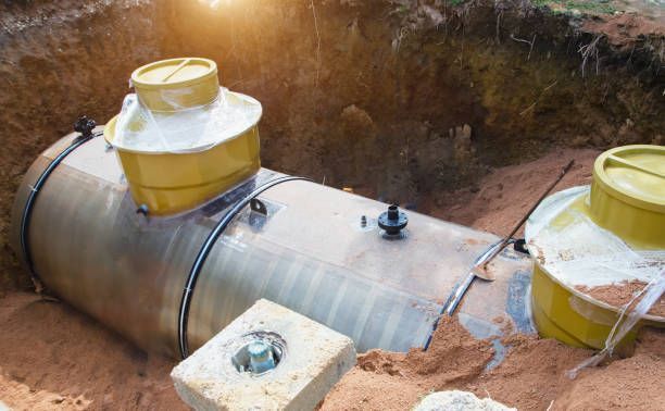 A metal underground storage tank with two yellow access ports, partially buried in dirt.