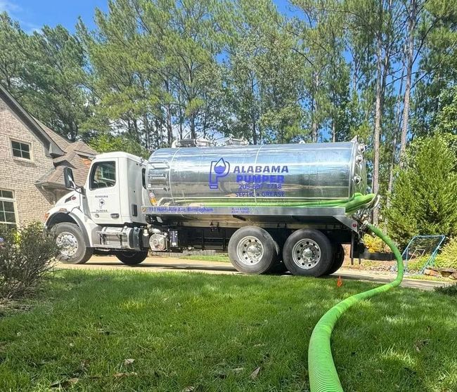 An Alabama Pumper tanker truck parked on a residential lawn, with a large green hose extending into the foreground.