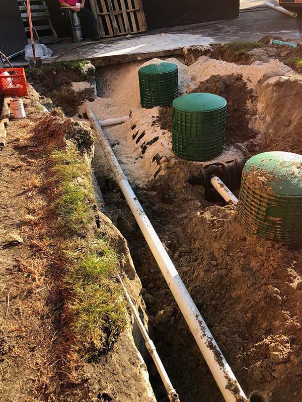 A trench containing white PVC plumbing pipes leads toward three green septic riser covers partially buried in soil.