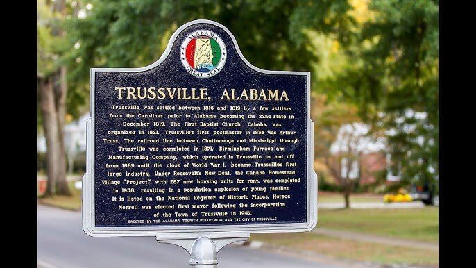 A black, metal historical marker for Trussville, Alabama, standing outdoors against a blurred, leafy background.