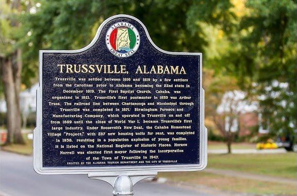 A black, arch-topped historical marker for Trussville, Alabama, standing outdoors against a blurred, leafy background.