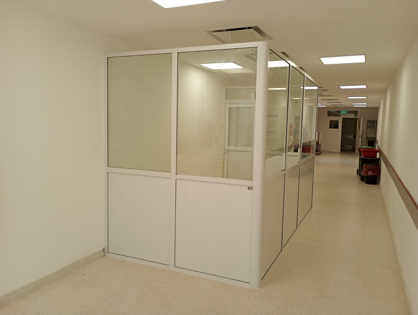Empty office hallway with white cubicle walls and beige carpet, lit by fluorescent ceiling lights