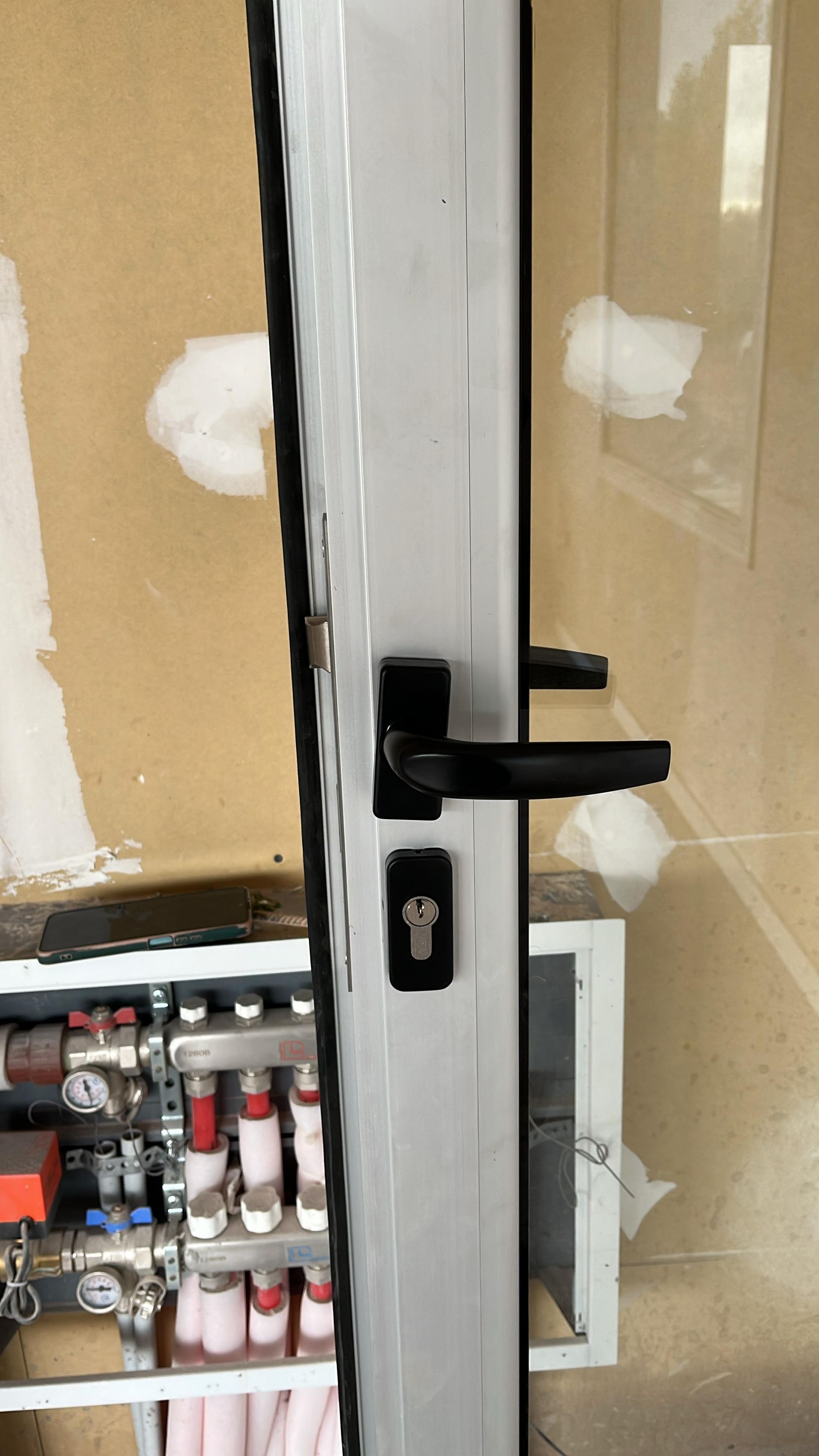Manilla y cerradura negras en una puerta de cristal, con estantes llenos de botellas pequeñas visibles en el interior.