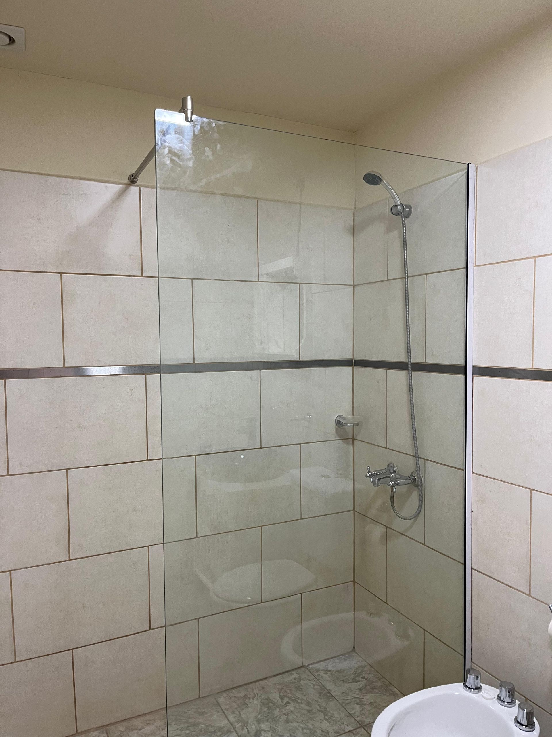 Tiled shower with glass partition, mounted showerhead, and built-in shelf in a bathroom.