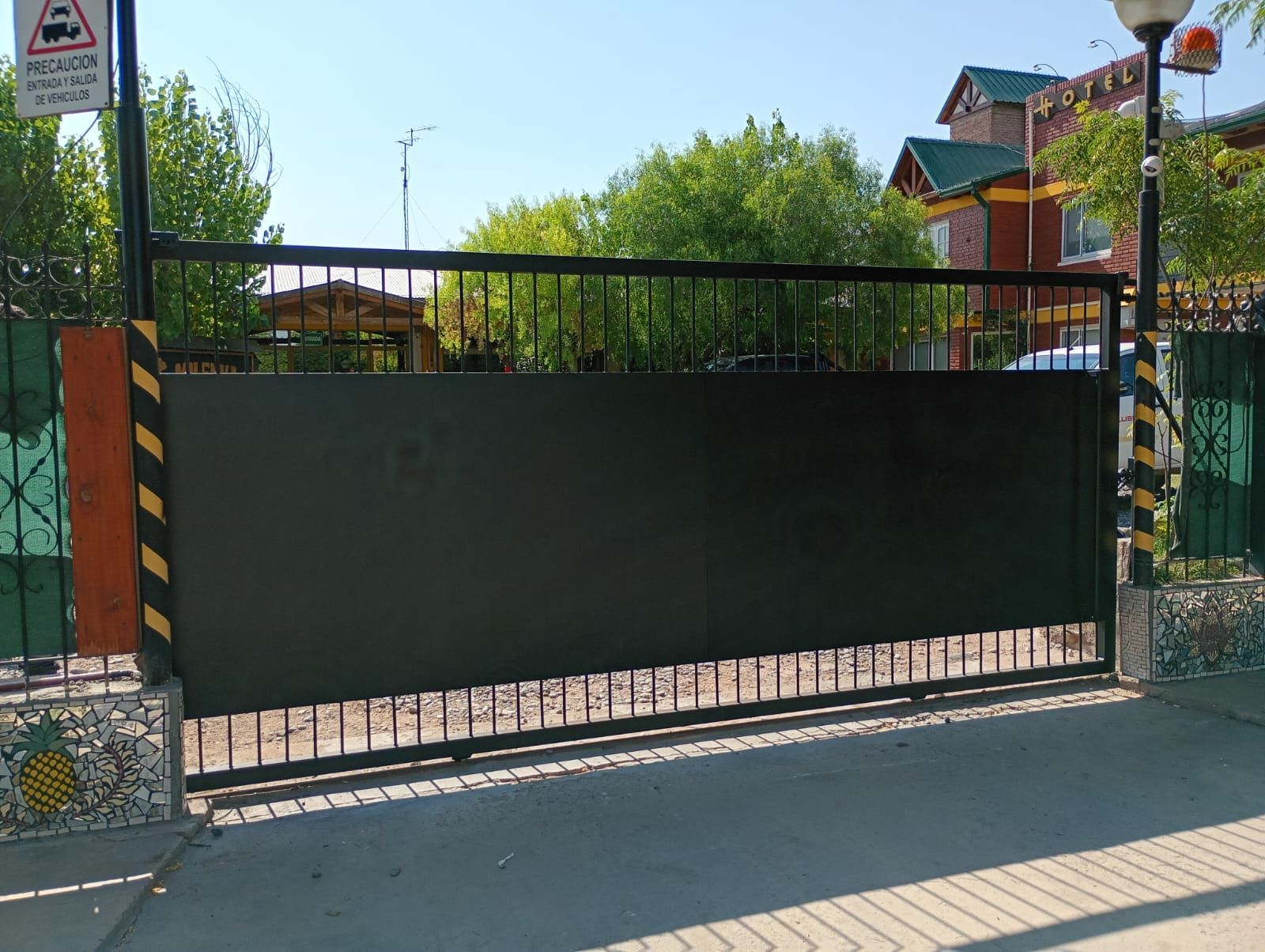 Closed black metal gate at the entrance to a park, with trees and playground structures behind it