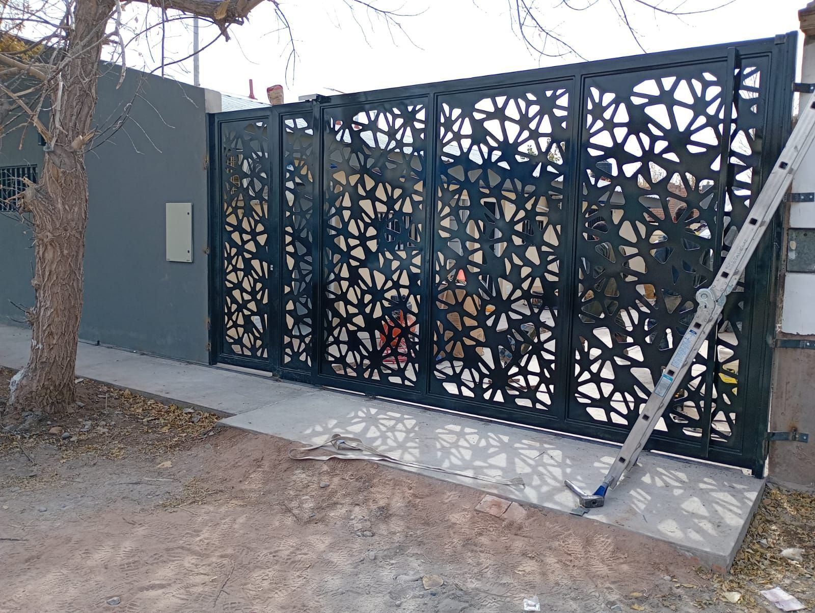 Black metal gate with abstract cutout design along a sidewalk beside a gray wall