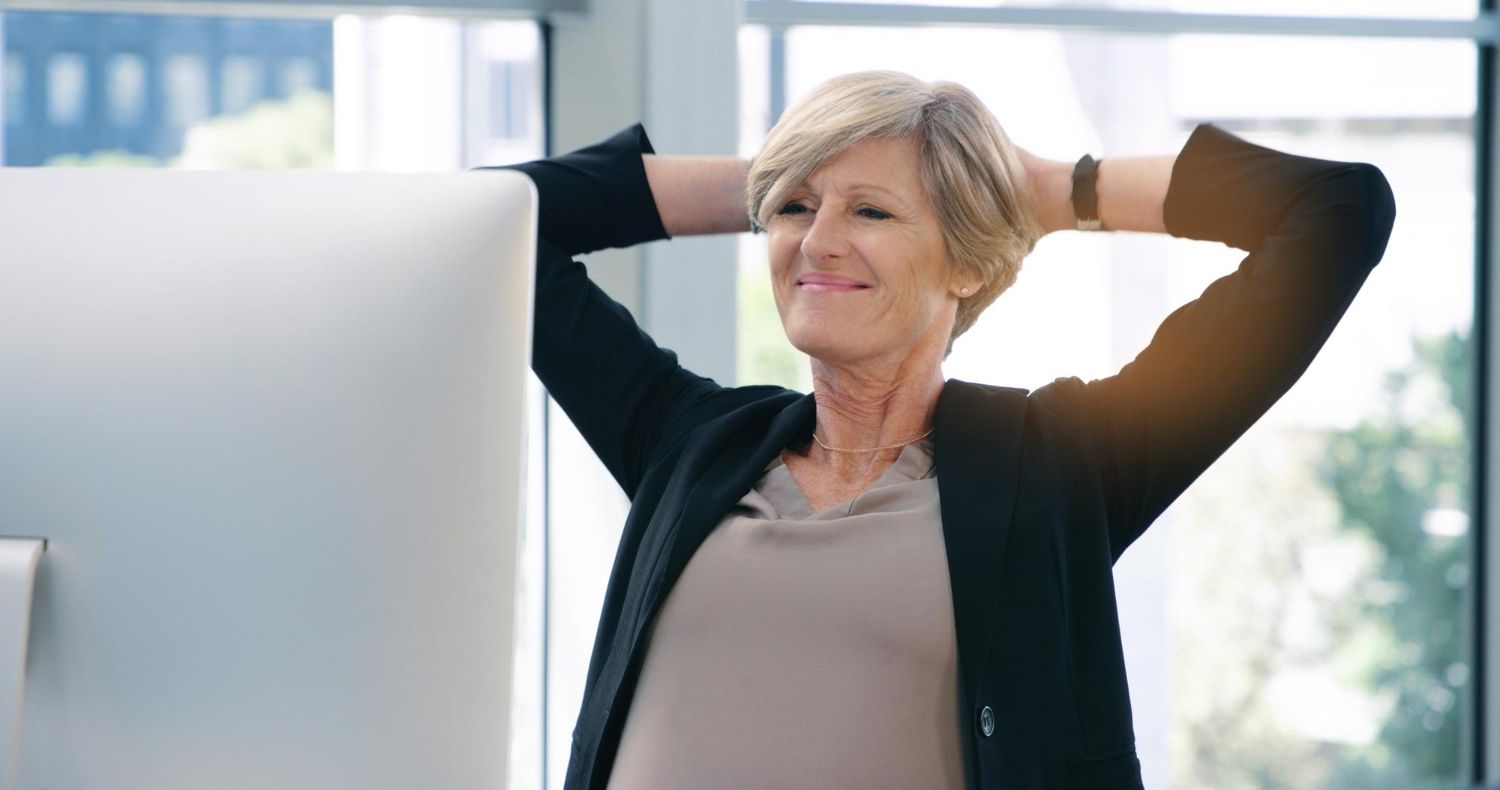 Smiling woman stretching with hands behind her head in a bright office