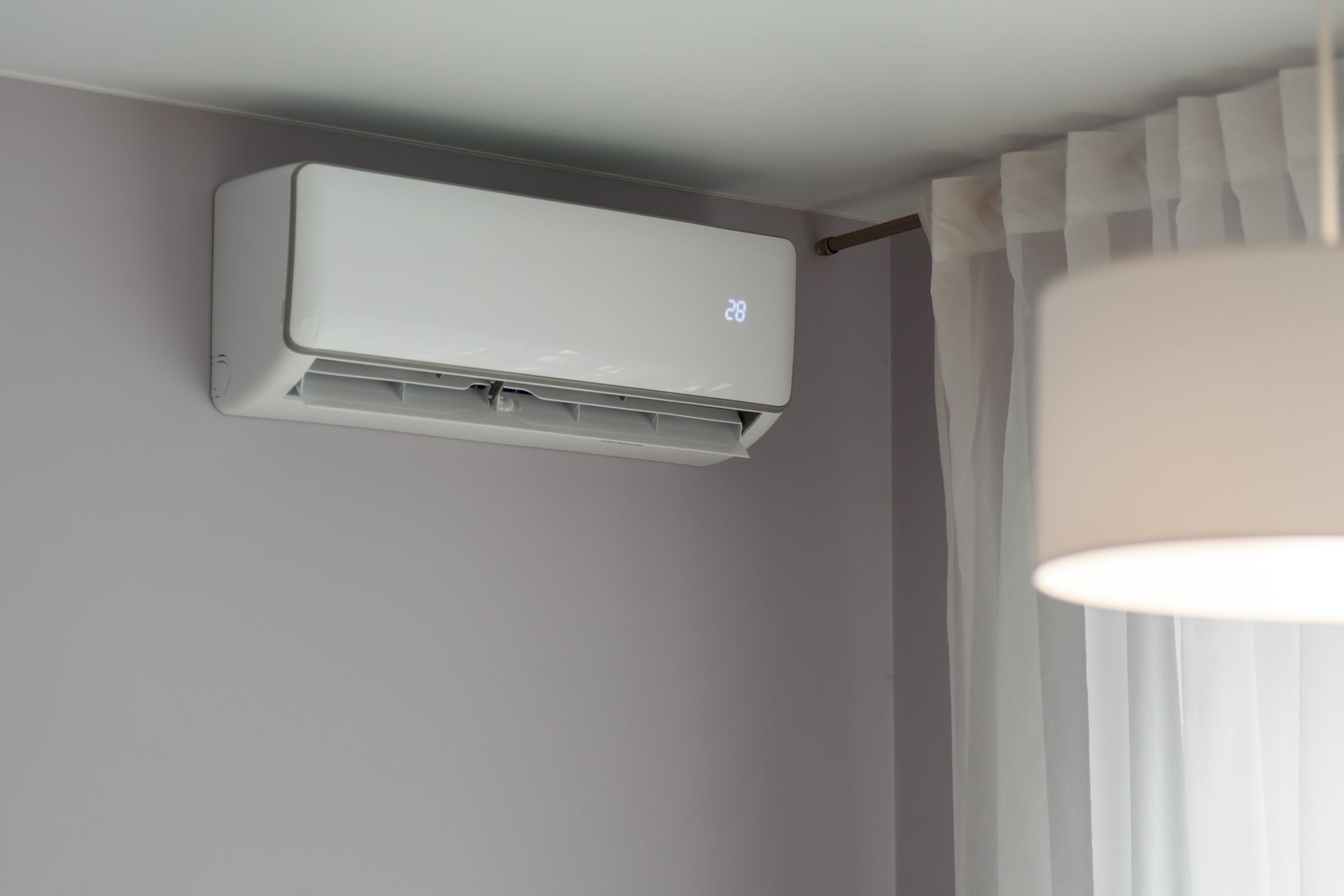 Wall mounted heat pump unit running inside a room with curtains and soft lighting. Wall mounted heat pump unit running inside a room with curtains and soft lighting.