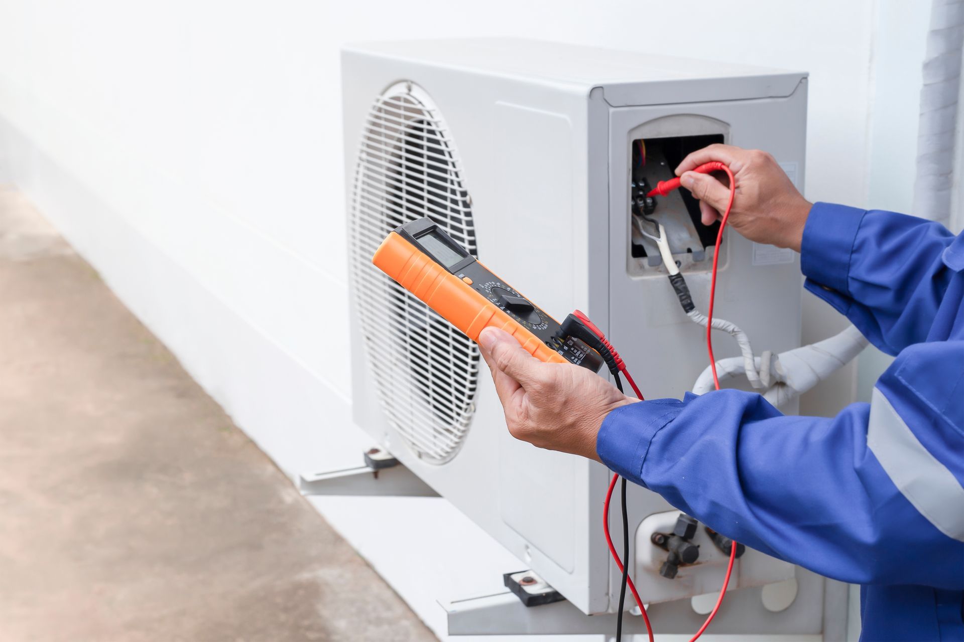 Heat pump installation technician testing outdoor unit with digital meter during system setup. Heat pump installation technician testing outdoor unit with digital meter during system setup.