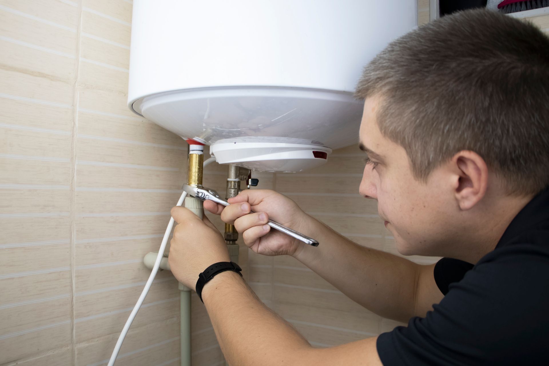 A male worker is repairing a water heater with a wrench.