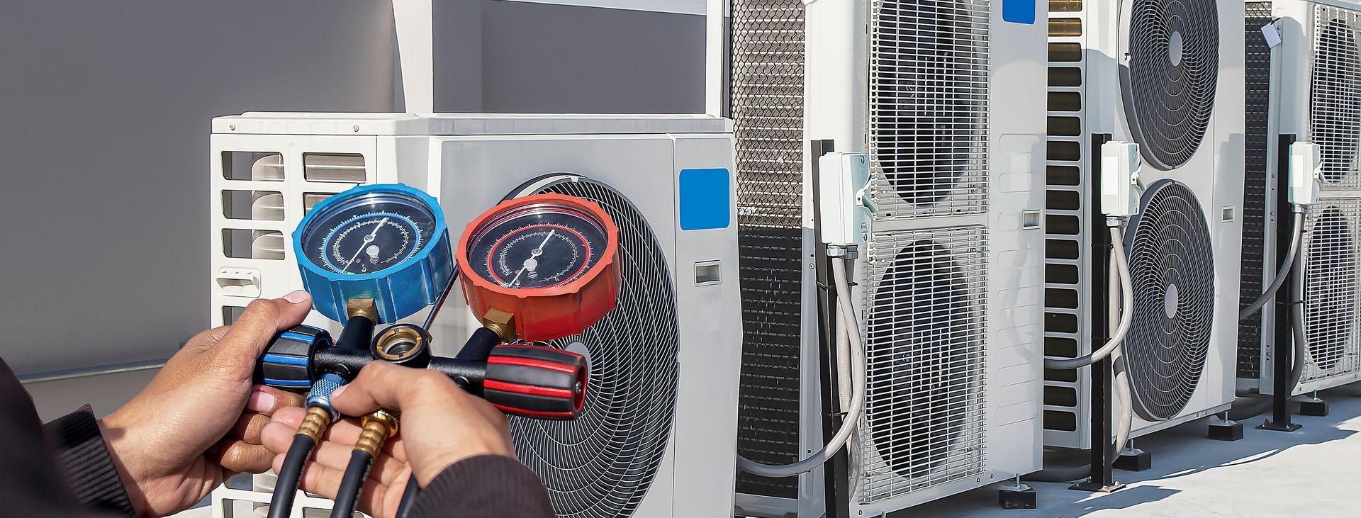 HVAC technician uses pressure gauges servicing outdoor air conditioning units for maintenance repair.