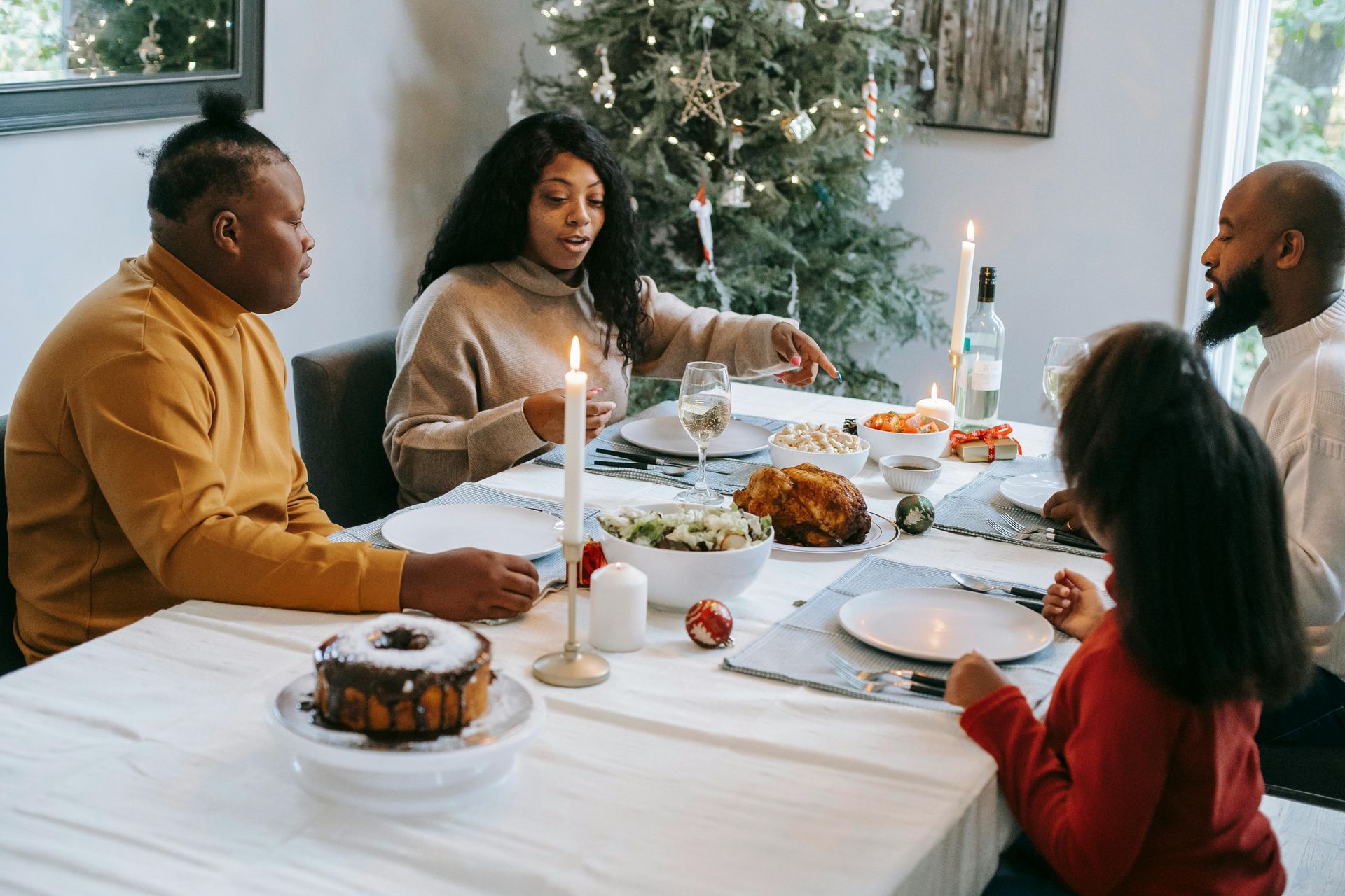 Family seated around a dining table, Christmas tree in background. Eating a meal with candles.