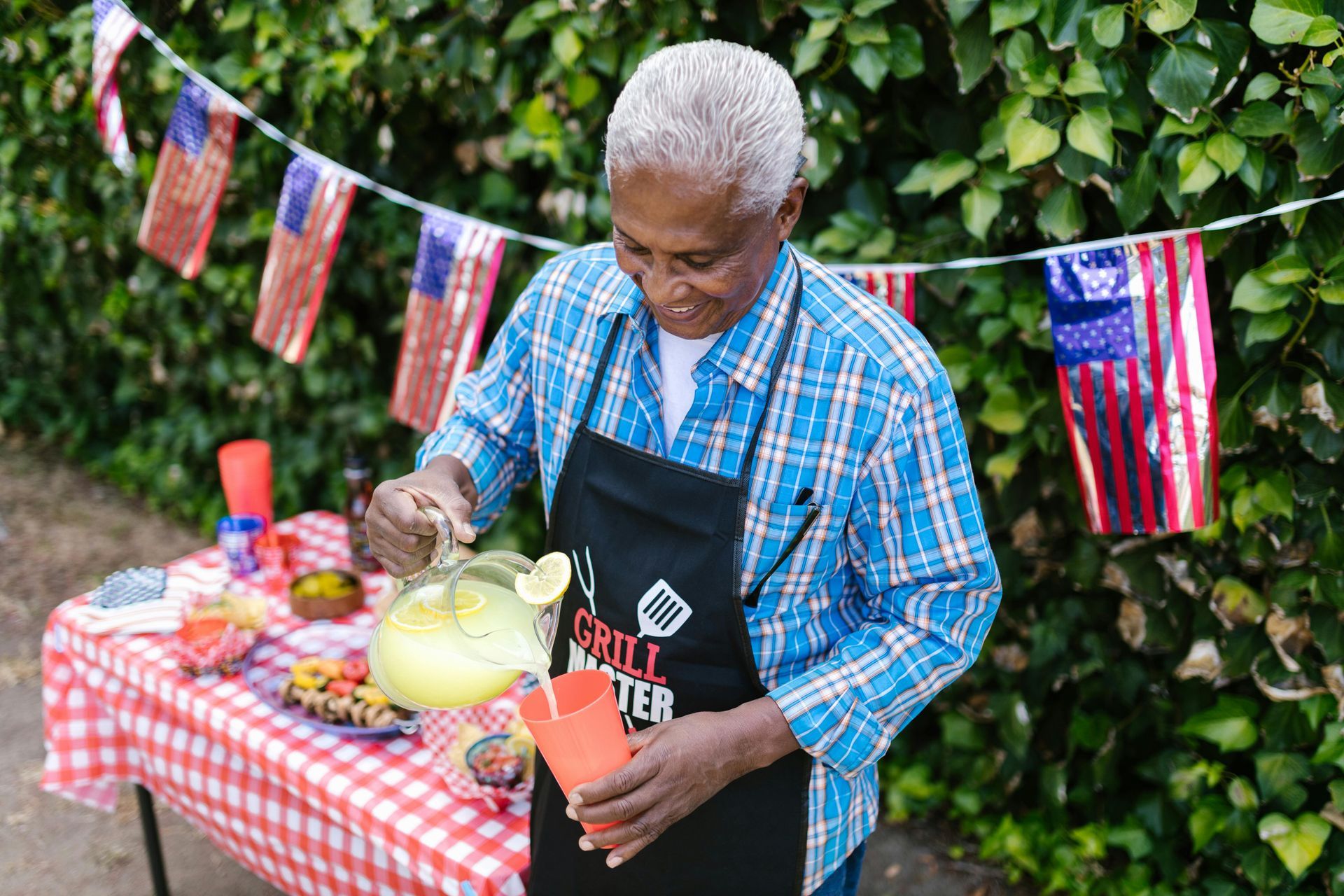 An elderly man is pouring a drink from a pitcher at a picnic table.