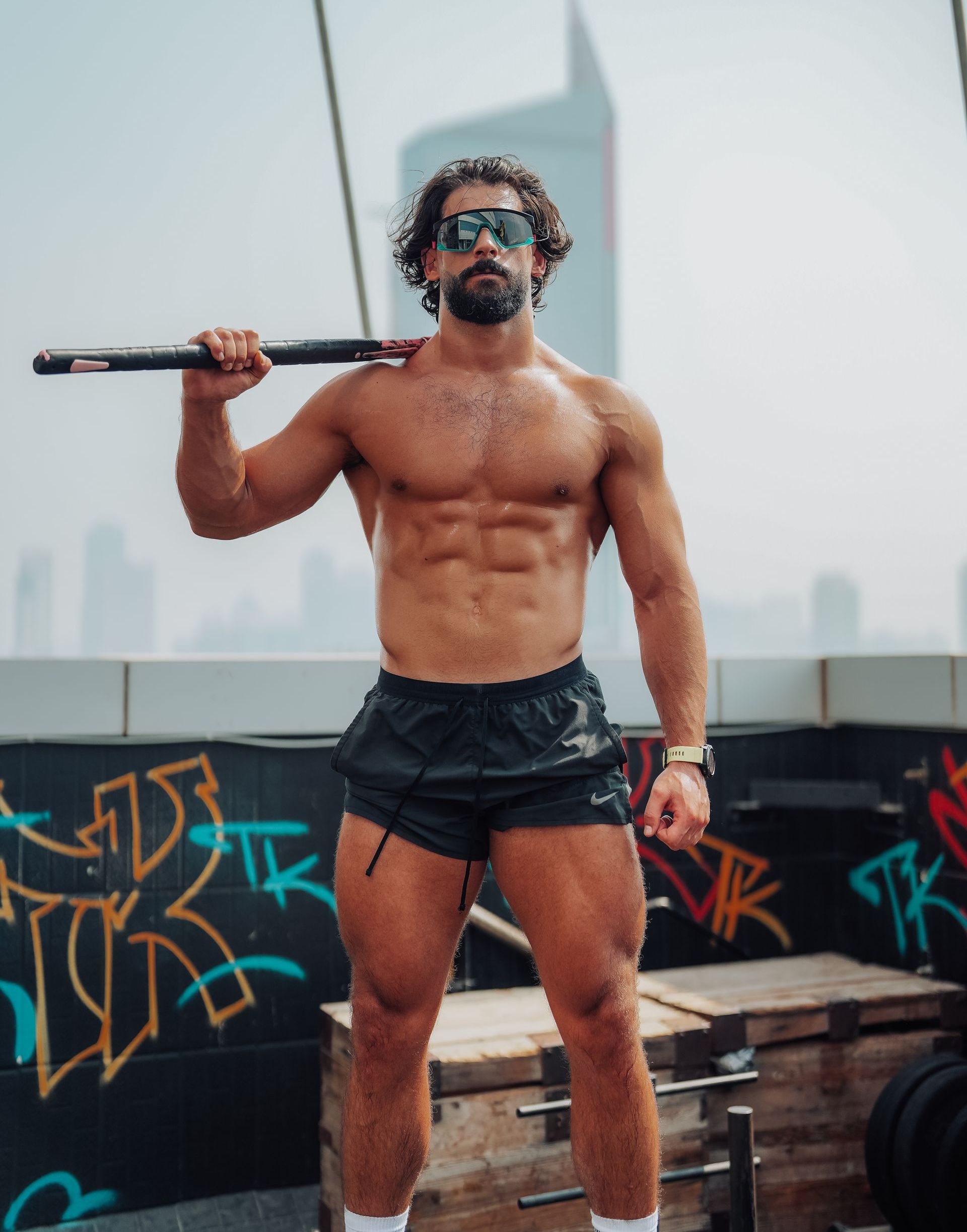 A shirtless man is holding a barbell over his shoulder