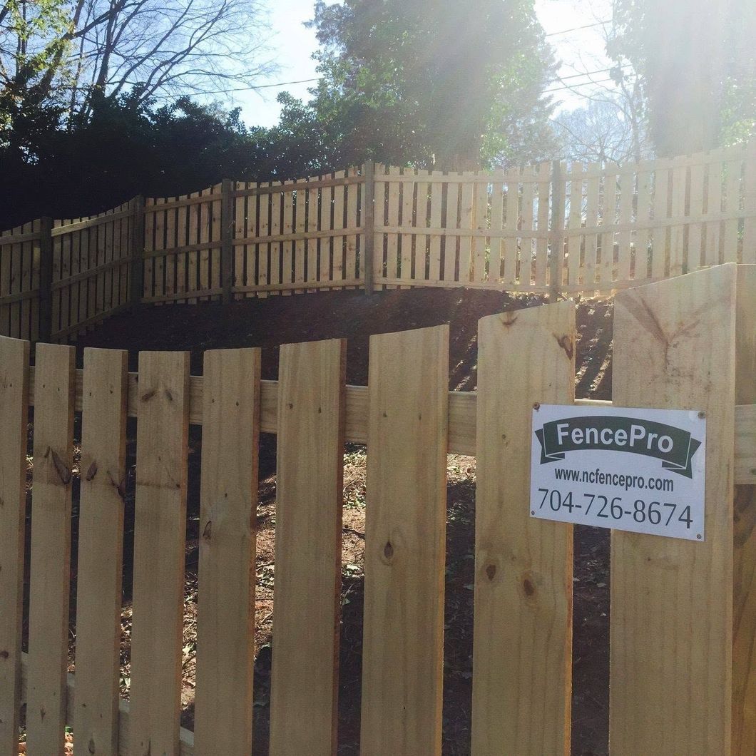 Wooden fence with a FencePro sign on a sunny outdoor slope.