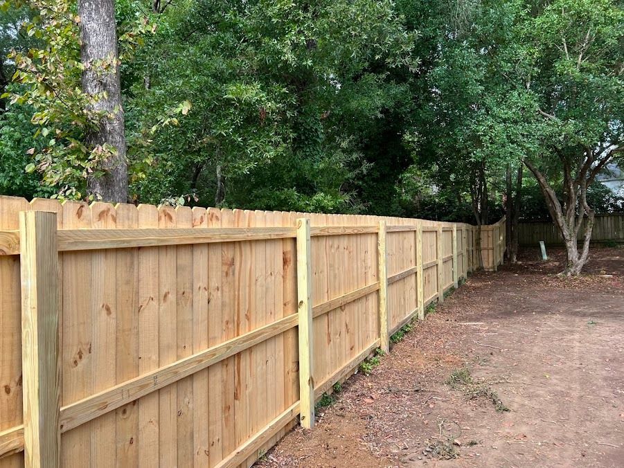 Wooden privacy fence along a dirt yard beside trees and greenery