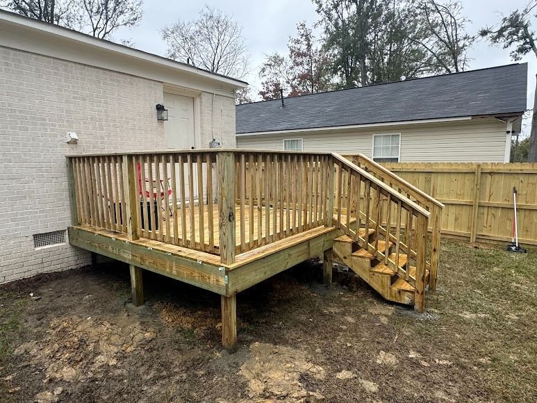 Wooden backyard deck with stairs beside a house, surrounded by a fenced yard.