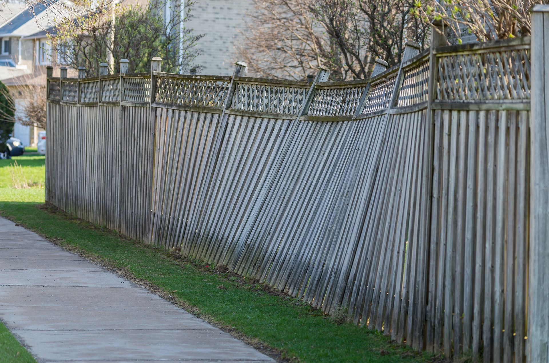 Wavy wooden fence along a sidewalk beside a grassy strip and houses