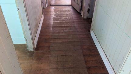 Narrow Hallway With Worn Wooden Floor and White Paneled Walls — The Good Wood Polished Timber Floors in Highfields, QLD