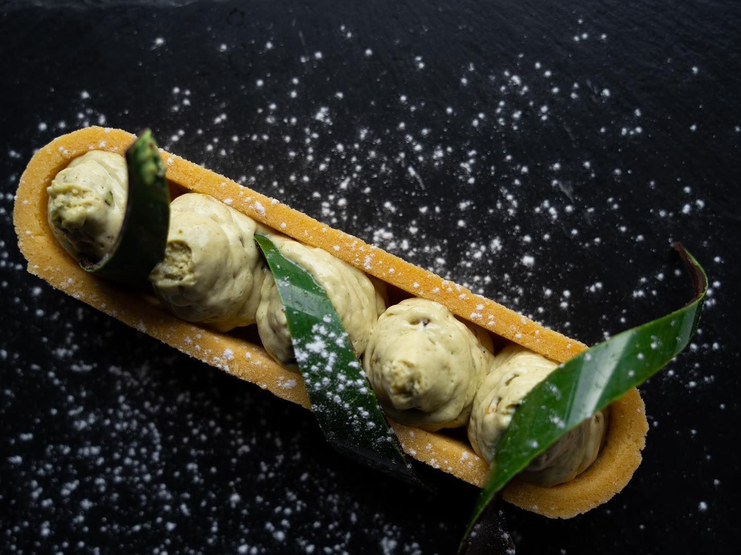 Dessert: palline di gelato al matcha in un lungo guscio di biscotto dorato, decorato con foglie verdi e zucchero a velo.