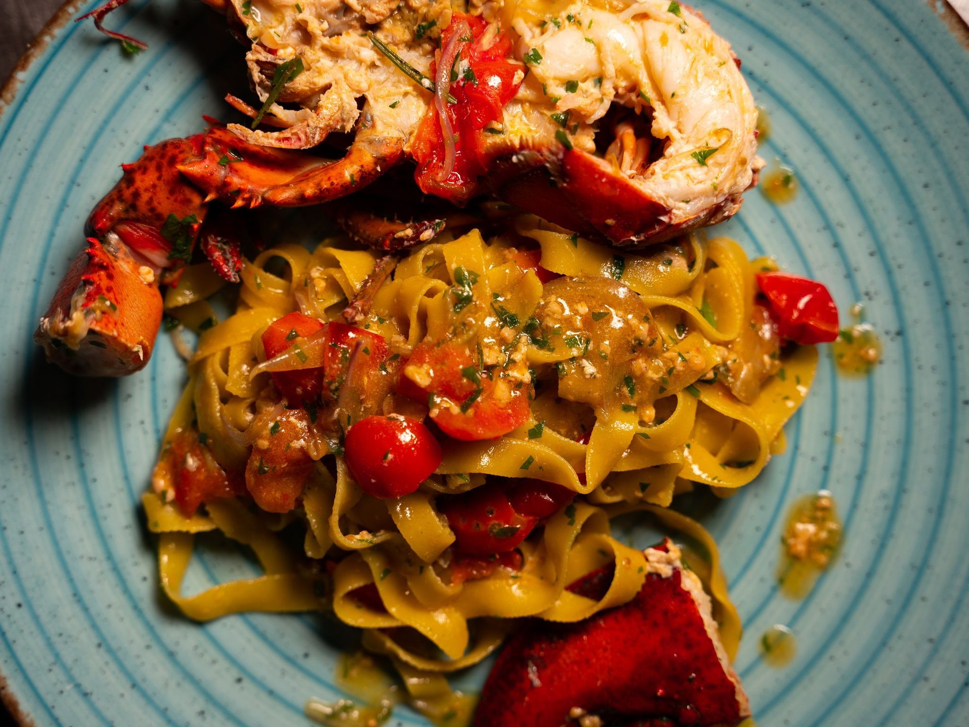 Piatto di pasta all'astice: astice cotto su pasta gialla con salsa di pomodoro, servito su un piatto turchese.