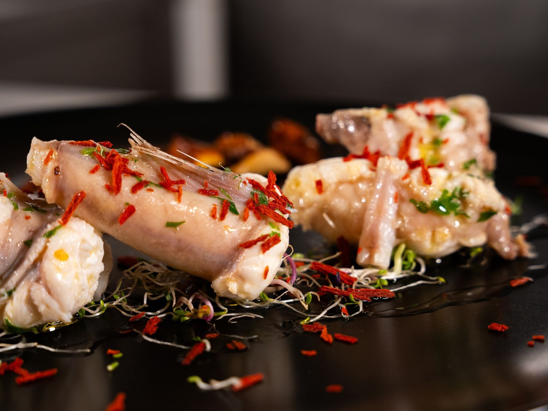 Primo piano di un piatto di frutti di mare con pesce bianco, spezie rosse e germogli su un piatto nero.