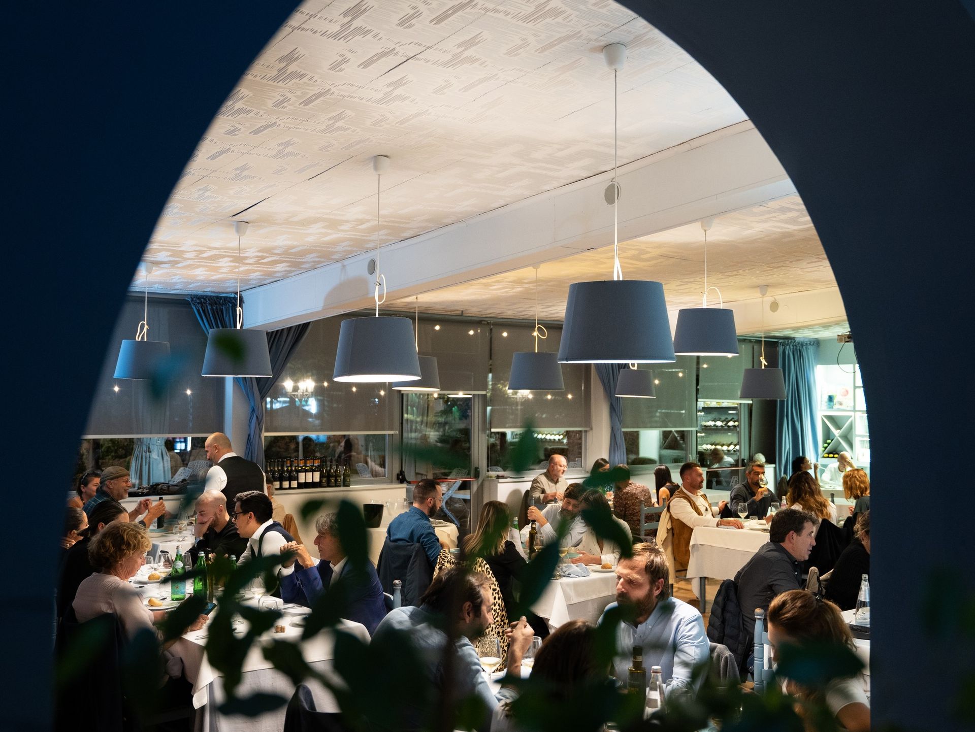 Interno di un ristorante con i commensali seduti ai tavoli sotto lampade a sospensione.