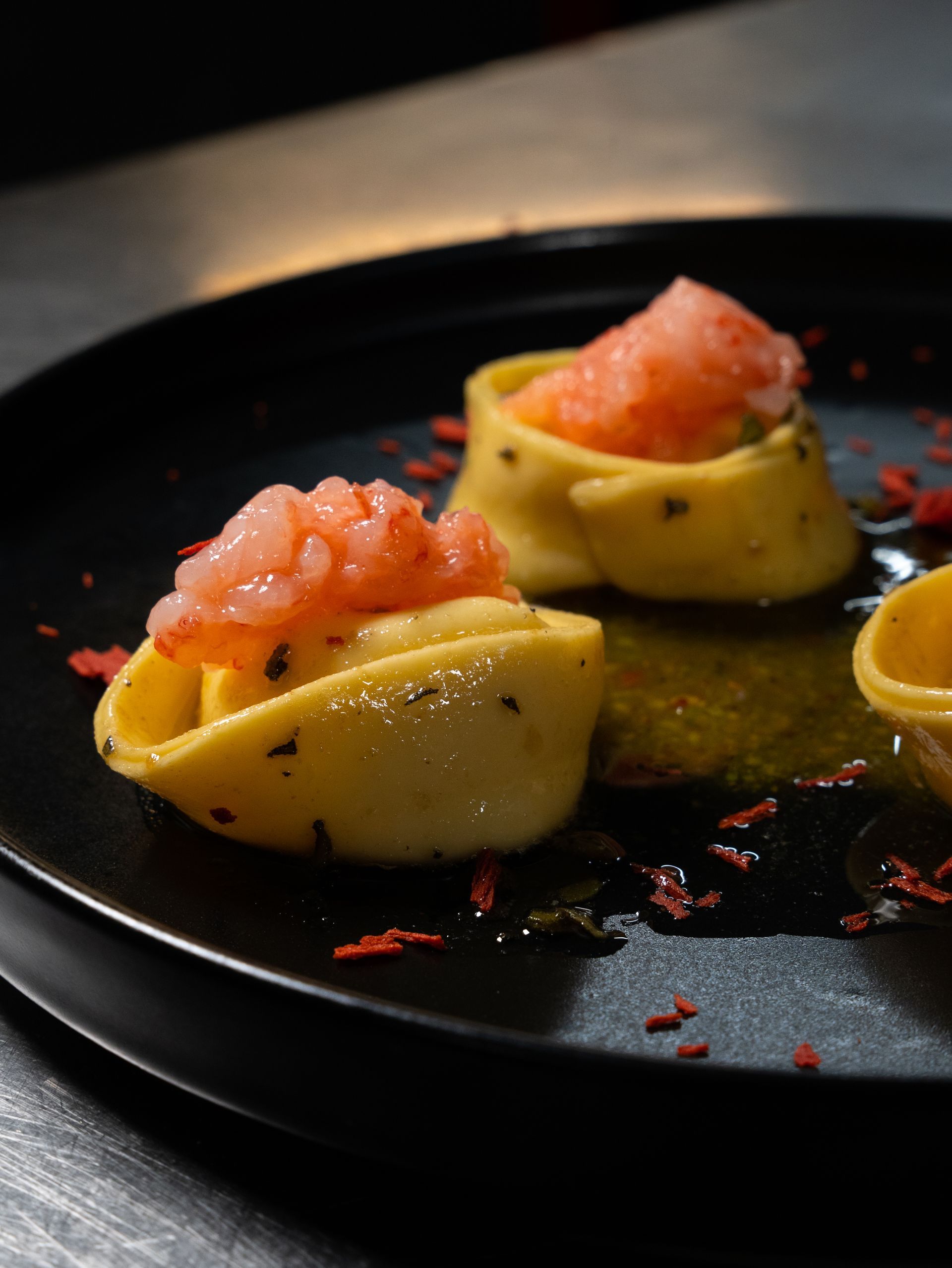 Primo piano di tre piatti di pasta con gamberi su un piatto nero. Pasta gialla e gamberi arancioni.
