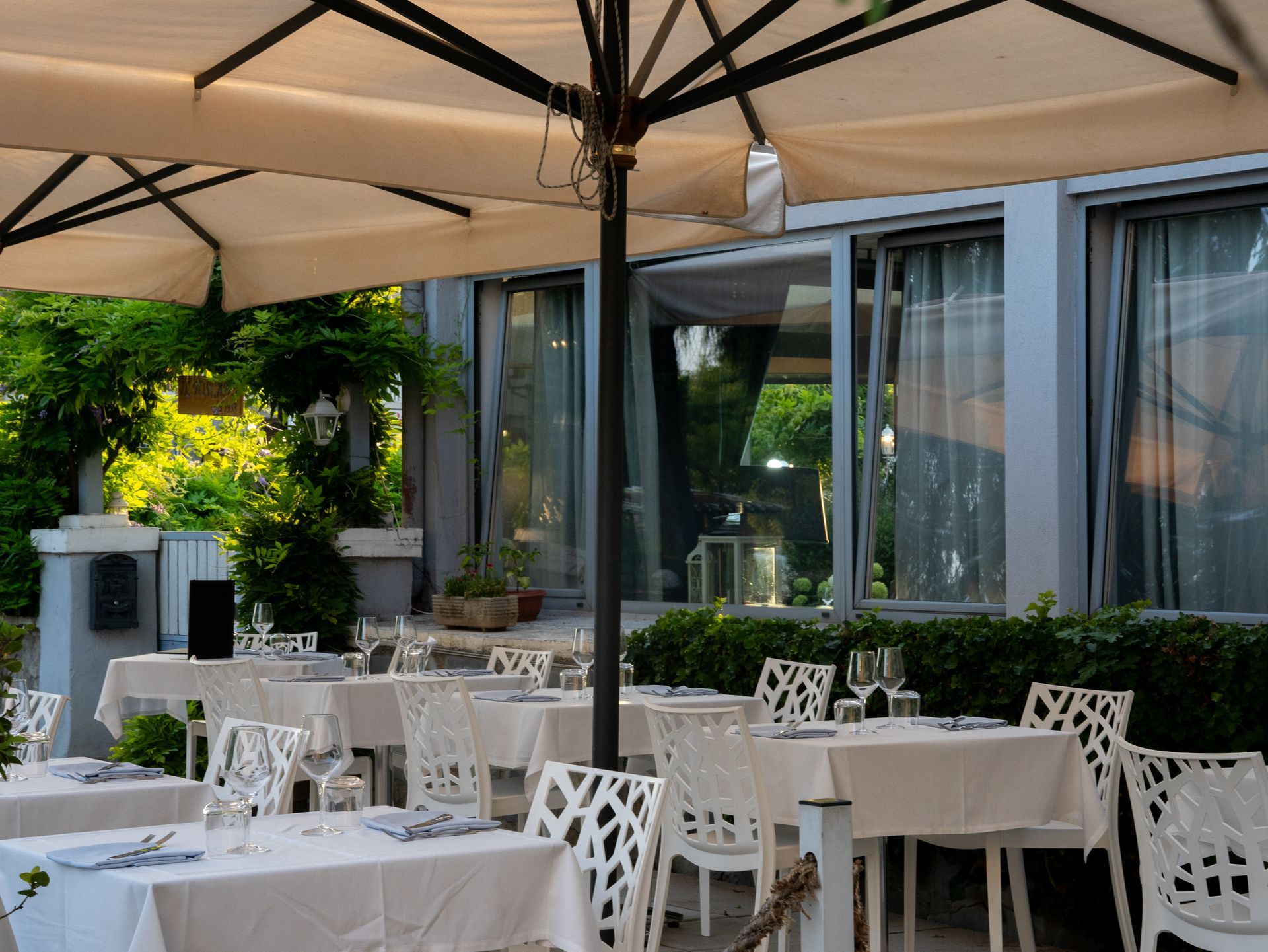 Patio esterno del ristorante con tavoli, sedie bianche e ombrelloni.