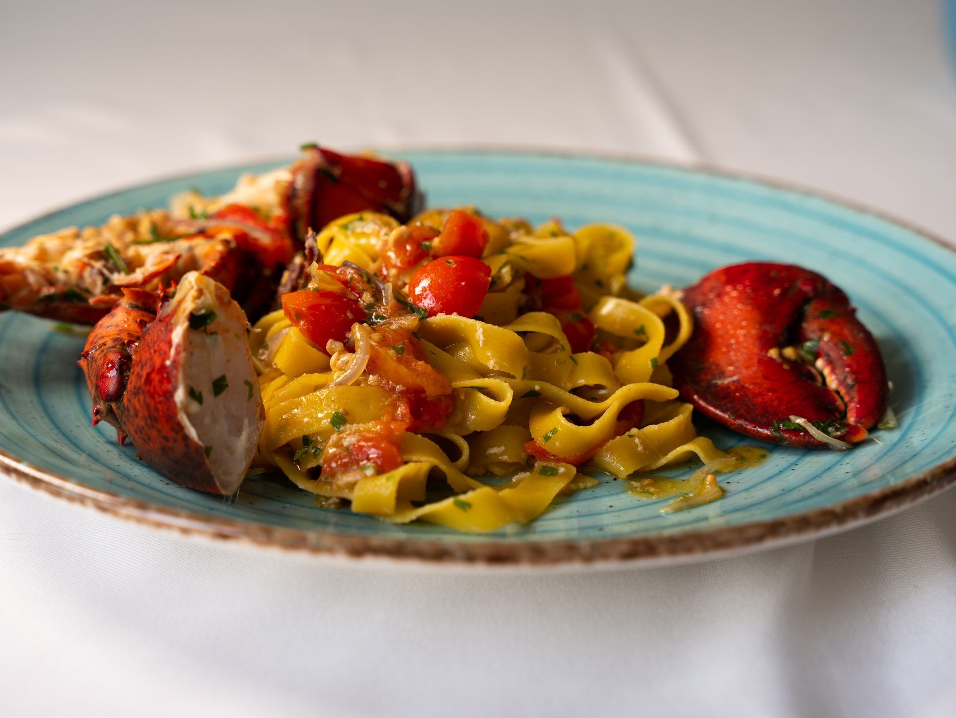 Pasta con chele di aragosta e salsa di pomodoro su un piatto blu.