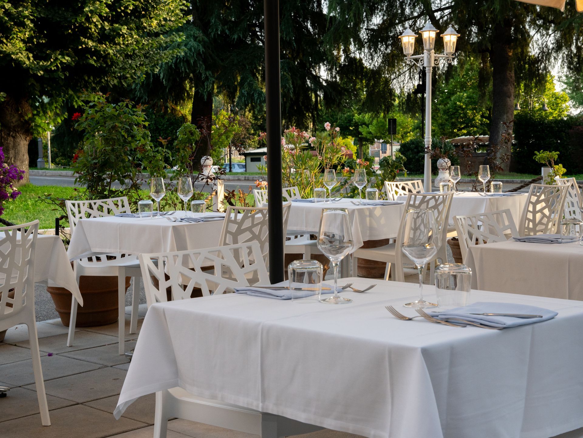 Tavoli da ristorante all'aperto apparecchiati con tovaglie bianche, sedie e bicchieri.