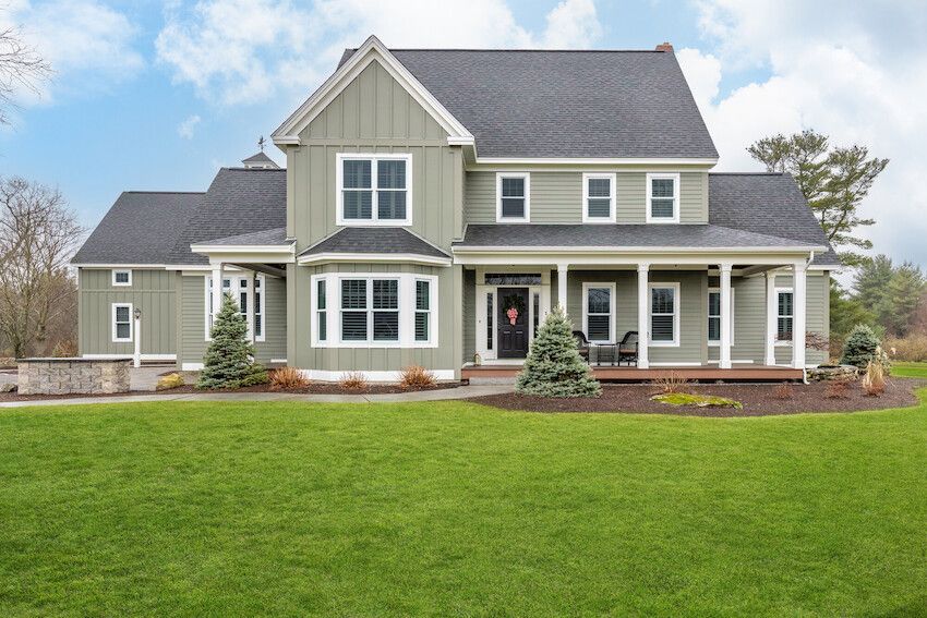 Two-story gray suburban house with white trim, covered porch, and a large green lawn