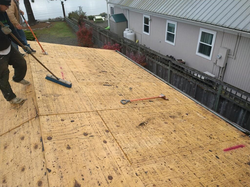 Workers installing plywood roof sheathing on a sloped roof beside a house