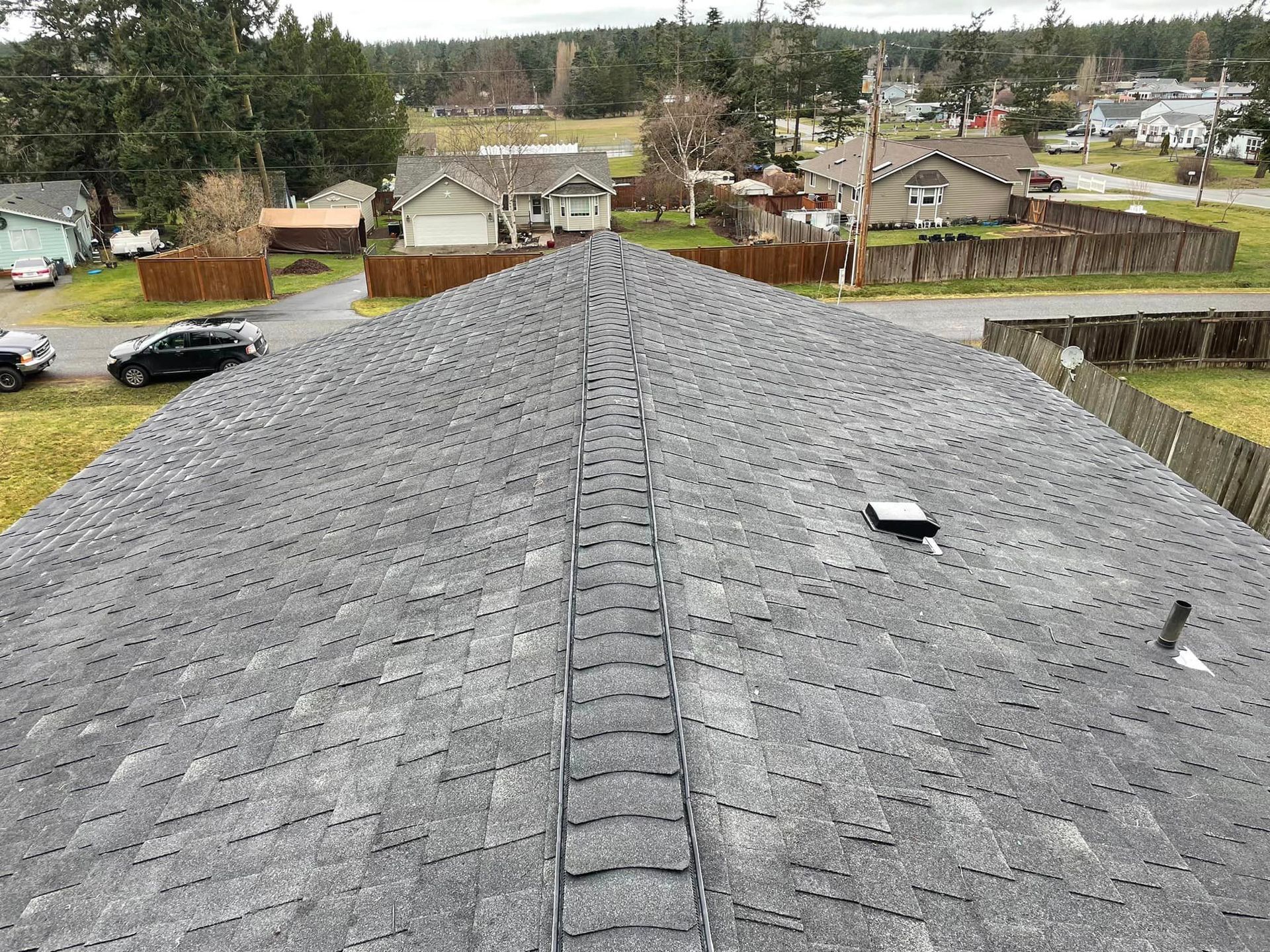 Gray shingled roof overlooking a suburban neighborhood with trees and houses