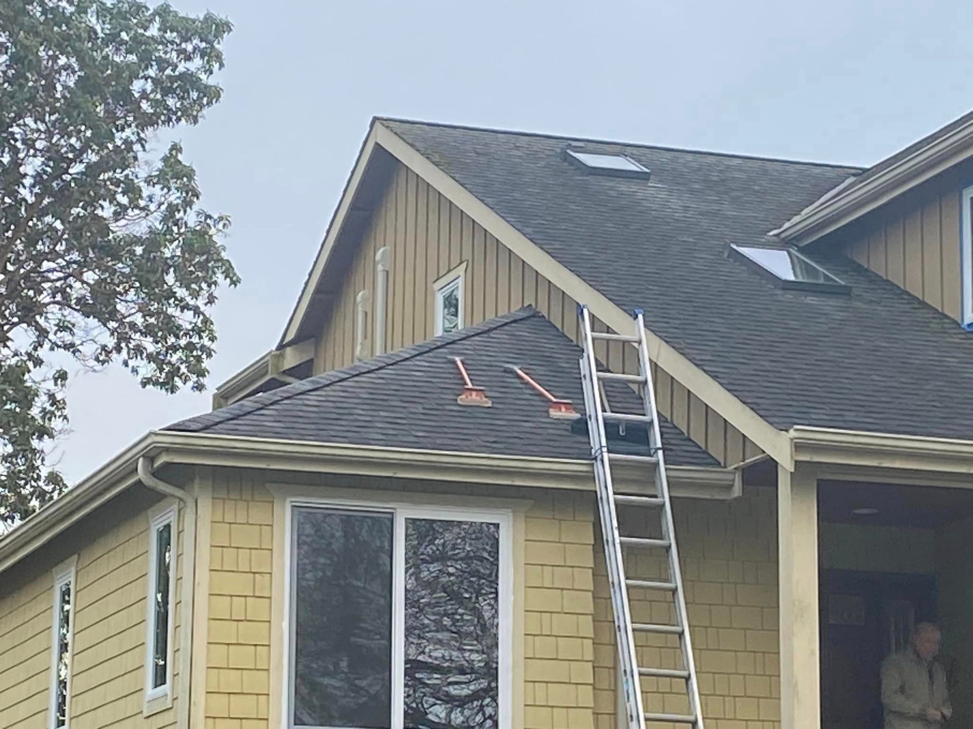 House exterior with a ladder against the roof, shingles being repaired, and a worker visible by the porch