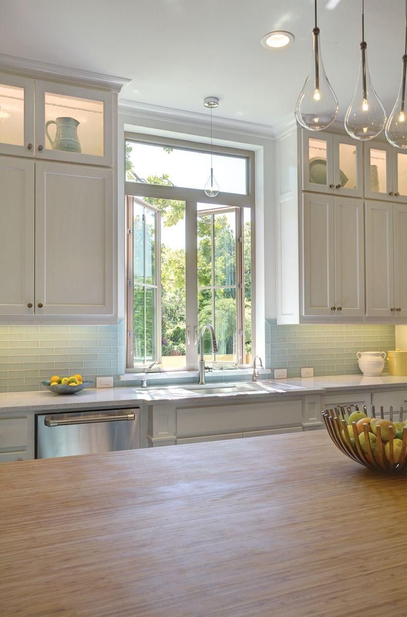 Bright white kitchen with large window, wood island, and hanging pendant lights