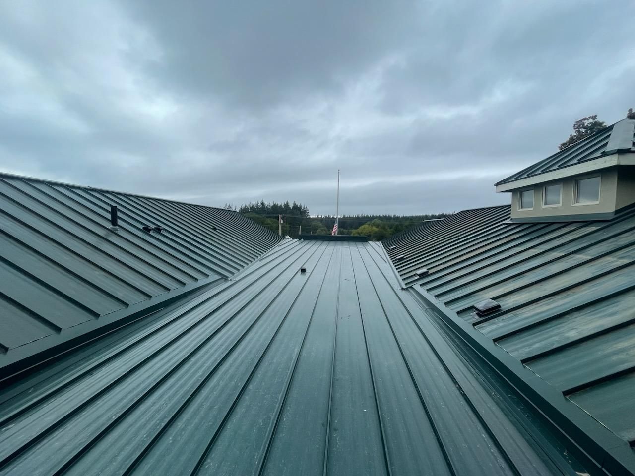 Metal roof valley under cloudy sky, with dormer windows on both sides