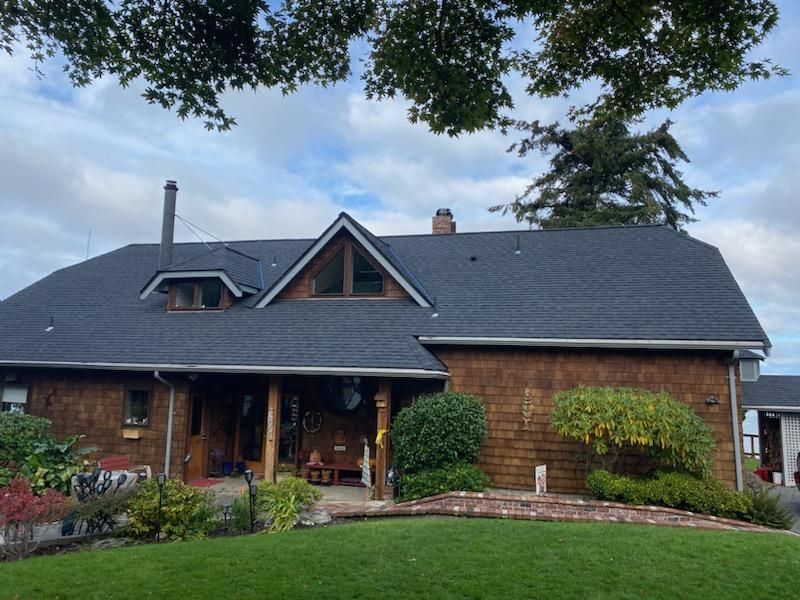 Brick house with dark roof, front porch, and landscaped garden under a cloudy sky