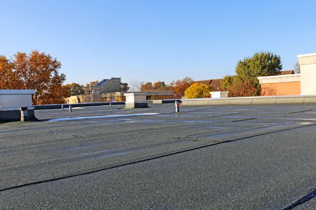 Flat rooftop with gravel surface, vents, and autumn trees under a clear blue sky.